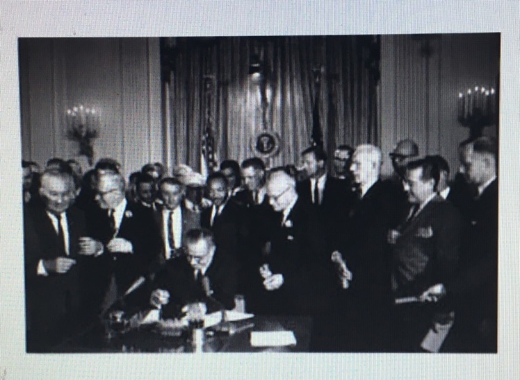 This picture shows Lyndon B. Johnson signing the Civil Rights Act in 1964. This law-example-1